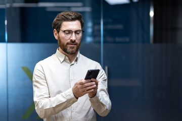 Young businessman standing in the office and using his mobile phone