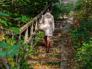 Clecy, Normandy, October 4, 2025. Autumn walk on forest steps. A woman in a coat and leather boots walks up forest steps in an autumnal setting. A charming scene depicting the tranquility of nature