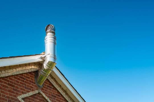 Shiny metal aluminium flue and rotating cover attached to a new central heating system. The large pipe extends to the gas fired heating system.
