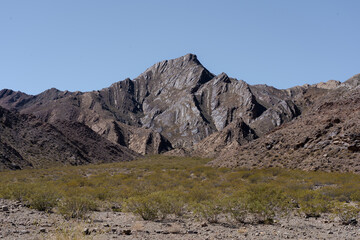 Folded mountain range in arid desert valley under clear blue sky