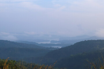 Misty morning view of Idukki dam reservoir from a distant hilltop, layers of green hills and blue water under a pale sky, perfect for scenic landscape and travel themes.
