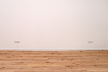 Empty room with white wall, wooden floor, and two electrical outlets. New home interior with natural light for renovation, real estate concept.