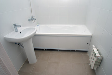 Minimalist white bathroom interior with bathtub, sink, and radiator. Modern home renovation and sanitary ware concept.