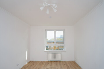 Empty bright room with white walls, wood floor, window, and radiator. Concept of a new apartment or home renovation.