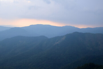 Naklejka premium Calm Kerala mountains at sunset, blue-toned hill layers in soft light and haze, evoking peaceful wilderness and travel inspiration
