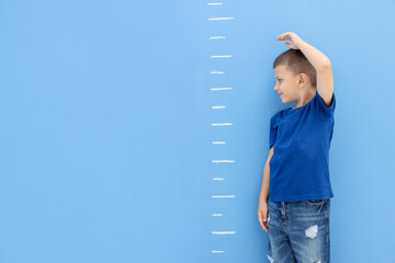 Little boy measuring his height near blue wall. Space for text