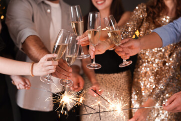 Friends celebrating New Year with sparklers and wine glasses indoors, closeup