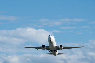 Airplane in the blue sky with white clouds on the background. A white airplane taking off against a backdrop of clouds.