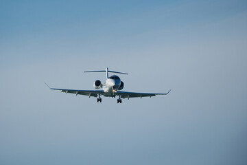 A private jet approaches the airfield against a backdrop of a partly cloudy sky. Airplane in the blue sky with white clouds.