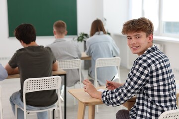 Students taking exam at wooden table indoors, selective focus