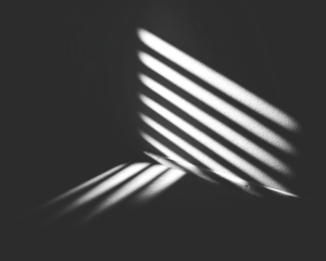 Dramatic light and shadow play through slatted blinds in a darkened space