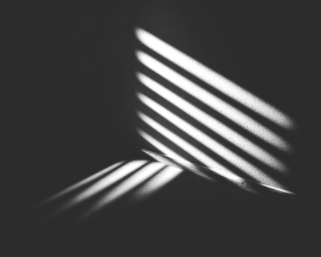 Dramatic light and shadow play through slatted blinds in a darkened space