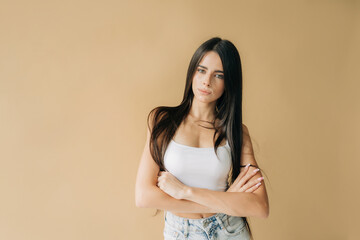 A beautiful slender young Caucasian woman with long black hair stands against a beige background.