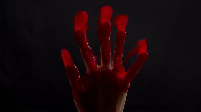 A hand covered in blood on glass. Horror, murder, and Halloween concept. Close-up of the red paint.