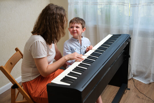 Woman teaches little boy playing piano at home. Child learning music lesson with teacher. Music education for kid. A child aged 4 years (four years old)