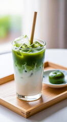 Fototapeta premium Iced matcha green tea latte with milk in a glass. Refreshing Japanese summer beverage on a wooden tray with a traditional sweet