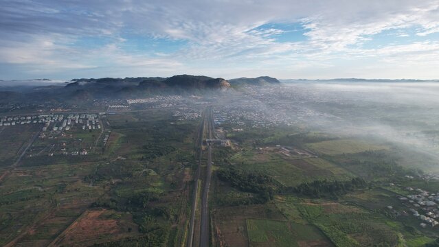 Aerial view of a sprawling city nestled beneath a majestic mountain range, veiled in a soft mist, contrasting with the lush greenery below, Ado Ekiti, Ekiti, Nigeria.