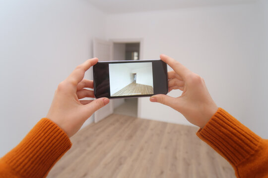 Woman holding smartphone to capture empty room for real estate listing or apartment search. Interior design and renovation concept.