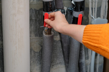 Woman turning red valve on pipe, controlling water supply. Energy efficiency and home renovation...