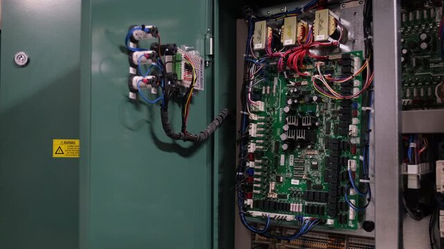 Open control panel with circuit boards wires and electrical components There is a warning sign on the side of the door and tubes