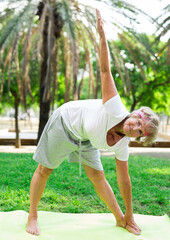 Old lady standing in triangle yoga pose outdoors