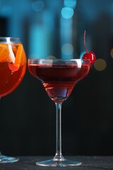 Glasses of tasty cocktails on dark table against blurred background, bokeh effect