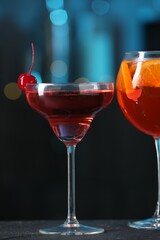 Glasses of tasty cocktails on dark table against blurred background, bokeh effect