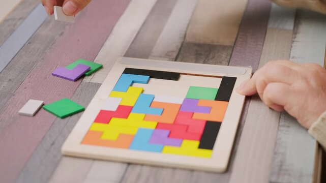 hands carefully placing colorful wooden geometric shapes intellectual puzzle, therapy cognitive training, dementia aid, brain health, occupational therapy, logical thinking, mental exercise
