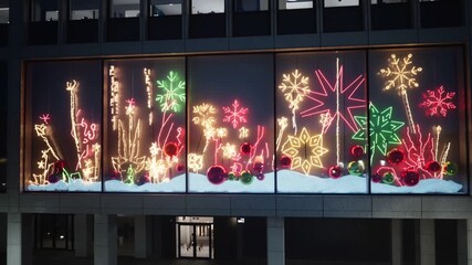Panning camera along nighttime street from building to row of windows, showing neon holiday display - Powered by Adobe