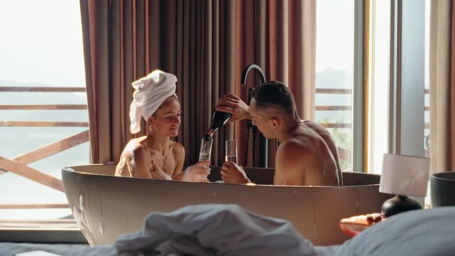 Romantic couple enjoying a hot bubble bath together while clinking champagne glasses in a rustic wooden cabin. Morning light pours in through the window, creating an intimate and serene atmosphere