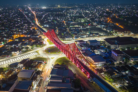 Aerial view of the Bekonang Bridge glowing red at night, connecting across the Solo River, with lights twinkling like stars in the cityscape, Surakarta, Central Java, Indonesia.