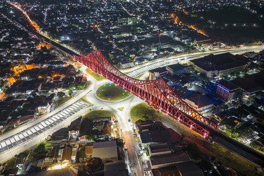 Aerial view of a red bridge illuminated against the night sky, with a roundabout and city lights creating a vibrant contrast, Surakarta, Central Java, Indonesia.