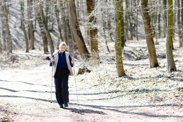 Young woman nordic walking in forest during winter sunny day