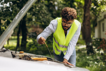 Man checking car engine oil level on roadside