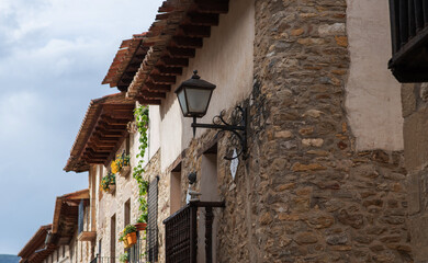 Rustic stone buildings line a narrow street in a charming Spanish village. The weathered facades...