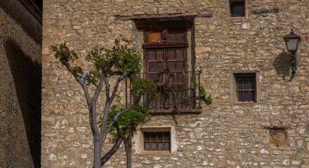 Fototapeta premium A weathered stone facade of a traditional Spanish building with wooden balconies and a wrought-iron lantern. Vines climb the structure, adding charm historic architecture