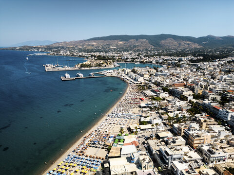 Aerial view of the sun-drenched beach meeting the turquoise sea, contrasted against the white buildings and the historic Neratzia Castle, Kos, Kos, Greece.