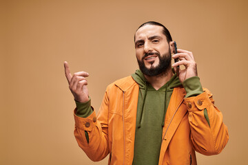 Stylish middle eastern man in green hoodie and orange jacket poses in studio setting