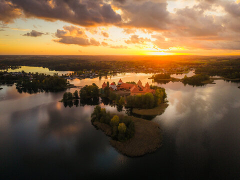 Aerial view of Trakai Castle bathed in the warm glow of the setting sun, its red brick contrasting against the deep blue waters of Lake Galve, Trakai, Lithuania.