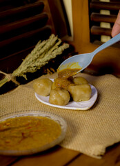 Close-up of cilok (Indonesian tapioca balls) served with spicy peanut sauce being poured using a spoon. The scene highlights the rich texture and flavor of traditional Indonesian street food.
