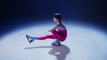 Female figure skater in pink suit performing sit spin on ice. Concept of meditative stillness, feminine discipline, graceful body control, modern sports minimalism, and quiet confidence.