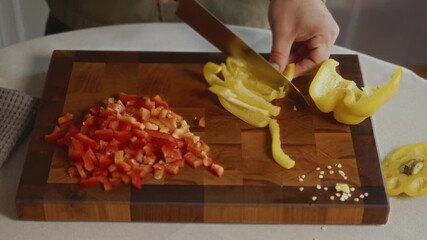 Man slicing yellow bell pepper on wooden cutting board with red pepper beside. Scene conveys cozy home comfort, minimalist lifestyle, and balanced daily cooking. High quality 4k footage - Powered by Adobe