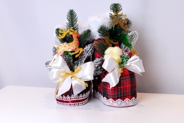 Pair of Christmas tartan boots decorated with fir branches, pinecones, golden glitter reindeer, white satin bows and festive ornaments. Winter New Year holiday home decor still life.