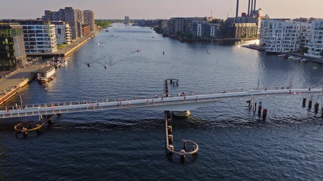 Aerial drone view of the Lille Langebro pedestrian bridge with people cycling and walking across the harbour at sunset in Copenhagen, Denmark
