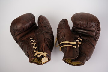 Vintage brown boxing gloves resting side by side on a plain background showcasing their worn leather texture and classic design