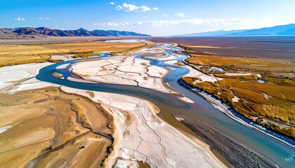 Aerial view of a wide river meandering through a dry arid landscape under a clear blue sky with distant mountains
