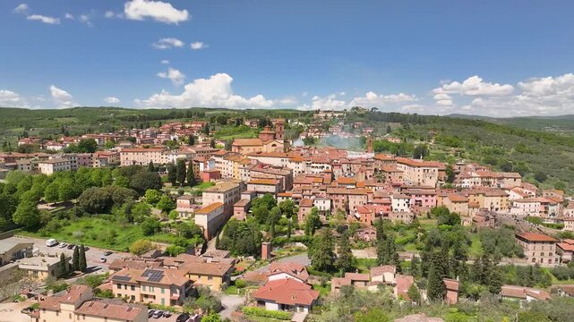 Aerial view of the town nestled among green hills, with red-tiled roofs contrasting against the lush greenery, Sinalunga, Tuscany, Italy.