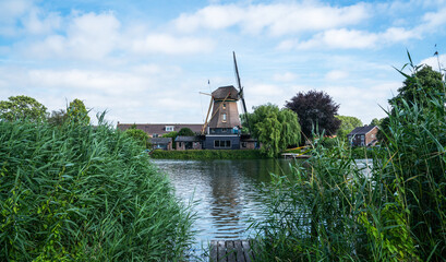 Thatched windmill and village houses on the riverbank in Aarlanderveen, South Holland, surrounded...