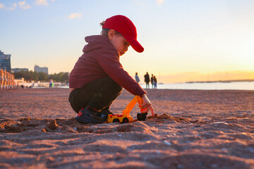 three-year-old boy plays with cars on the sand at the beach by the sea