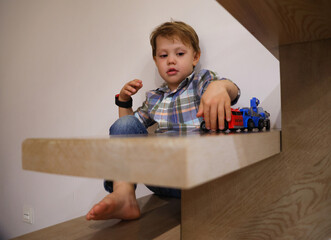 little three-year-old boy plays with cars alone on the stairs of his house